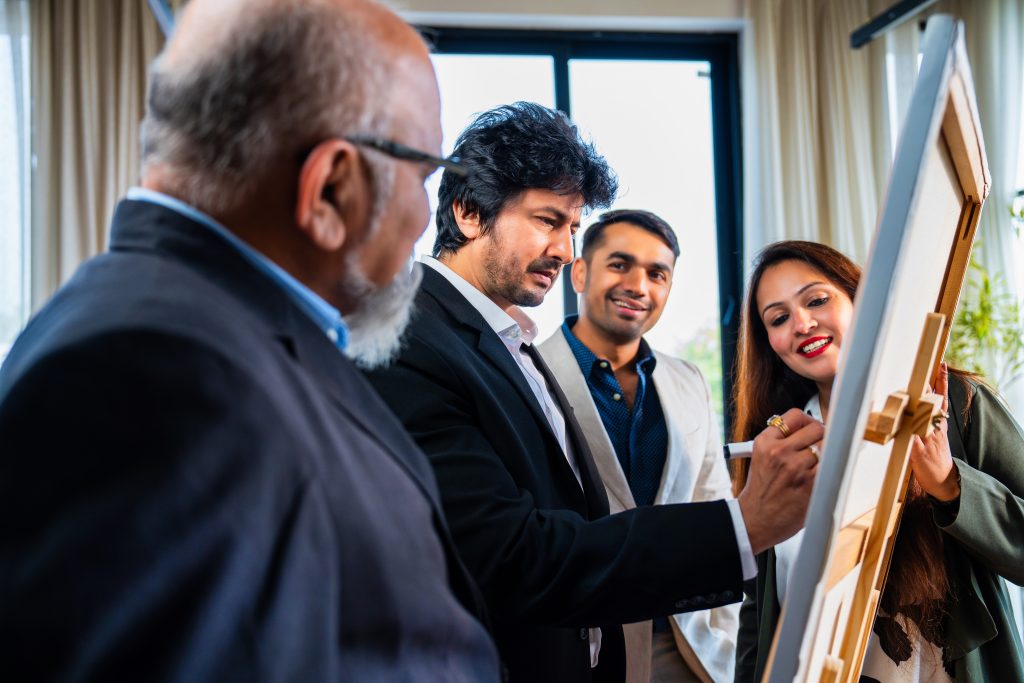 indian asian young businessman presenting strategy on whiteboard to colleagues in a corporate office